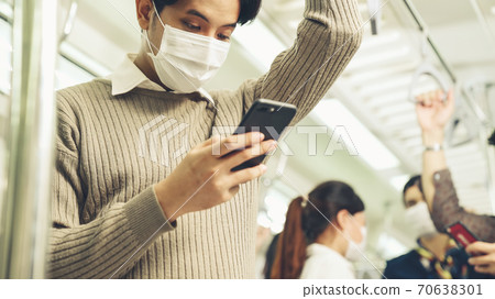 Traveler wearing face mask while using mobile phone on public train 70638301