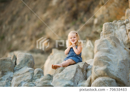 little girl sitting on rock at sunset. travel. 70638483