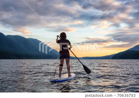 Woman Paddleboarding on Scenic Lake at Sunset 70638783