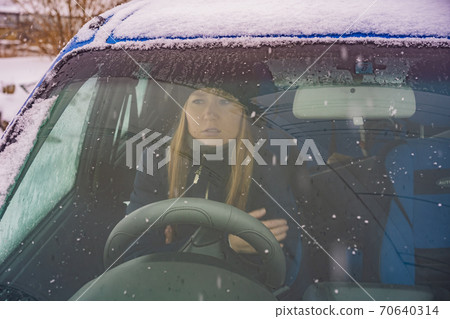 Woman in a car during a snowfall. It's cold, a woman wants to go on vacation, but can't because of quarantine COVID 19 70640314
