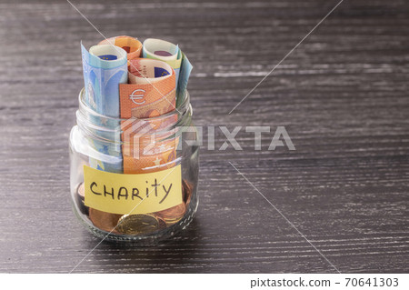 Glass jar with coins and euro notes with the inscription CHARITY. On the old black wooden table. The concept of kindness and help. 70641303