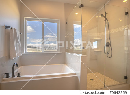 Built in square bathtub inside a bathroom with white wall and sliding window 70642269