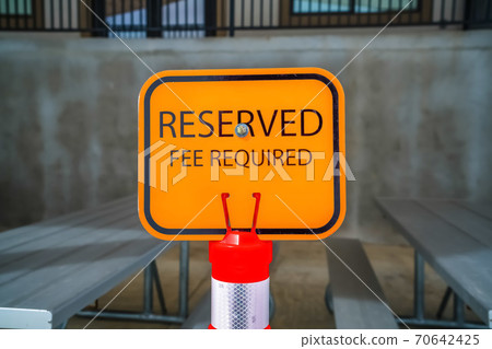 Close up of an orange Reserved sign with tables and benches in the background 70642425