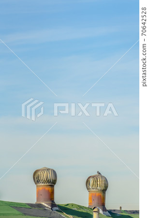 Green roof with metal turbine ventilator against cloudy pale blue sky Green roof with metal turbine ventilator against cloudy pale blue sky 70642528