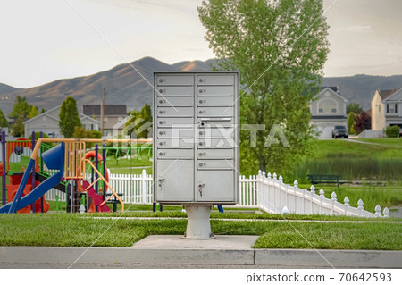 White metal cluster mailbox on the sidewalk in front of a colorful playground White metal cluster mailbox on the sidewalk in front of a colorful playground 70642593