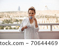 young beautiful Asian girl in beige lace shorts,white shirt drinking coffee standing on the balcony. selective focus. small focus area. 70644469