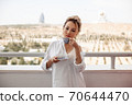 young beautiful Asian girl in beige lace shorts,white shirt drinking coffee standing on the balcony. selective focus. small focus area. 70644470