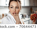 young beautiful Asian woman in beige lace shorts,white shirt eating grapes in the kitchen . selective focus: a small area of focus. 70644473