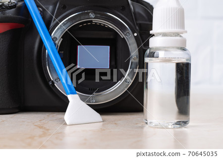 Dslr camera with raised mirror, liquid sensor cleaner and swab on a table. 70645035