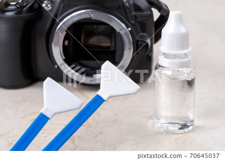 Liquid sensor cleaner and two swabs against dslr camera with lens removed. 70645037