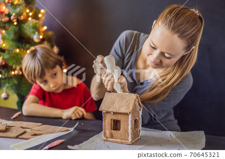 Young mother and kid making gingerbread house on Christmas eve Young mother and kid making gingerbread house on Christmas eve 70645321