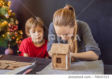 Young mother and kid making gingerbread house on Christmas eve Young mother and kid making gingerbread house on Christmas eve 70645323