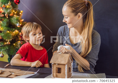 Young mother and kid making gingerbread house on Christmas eve Young mother and kid making gingerbread house on Christmas eve 70645325