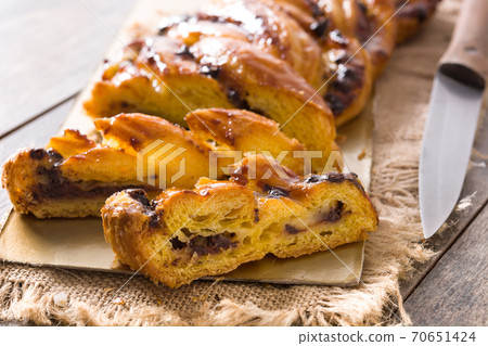 Homemade braid stuffed with chocolate and cut into pieces on wooden table. 70651424