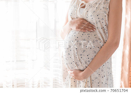 Pretty young pregnant woman standing by the window in home 70651704