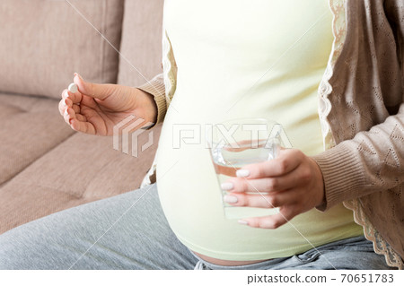 pregnant woman is sitting in sofa. Taking pills from colds. Last months of pregnancy 70651783