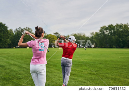 Two athletes practicing golf swings on the driving range 70651882