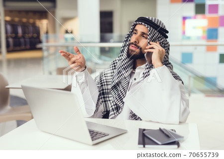 Young Arabian Man Using Phone and Laptop in Cafe. 70655739