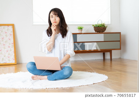 A young woman with a troubled face looking at a laptop while cross-legged in the living room A young woman with a troubled face looking at a laptop while cross-legged in the living room 70655817