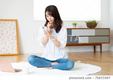 看她的智能手機的一個微笑的少婦在客廳 70655987