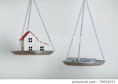 House model and money on balance scale watch. Choice concept. Investing money real estate or cash House model and money on balance scale watch. Choice concept. Investing money real estate or cash 70658253