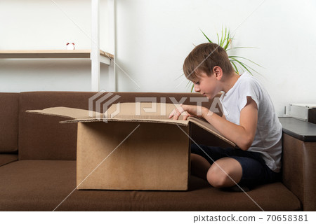 Boy looks into large open box. Child is unpacking large gift. 70658381