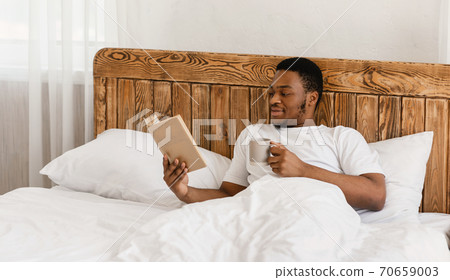 Black Millennial Guy Reading Book Drinking Coffee Lying In Bed Black Millennial Guy Reading Book Drinking Coffee Lying In Bed 70659003