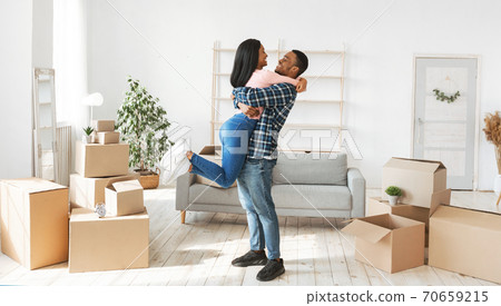 Home relocation concept. Happy black guy hugging and lifting his lovely wife in their new apartment, panorama Home relocation concept. Happy black guy hugging and lifting his lovely wife in their new apartment, panorama 70659215