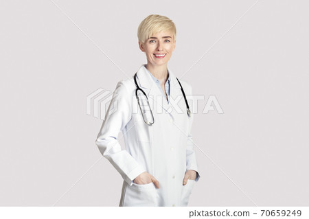 Attractive adult woman in white coat with stethoscope, puts hands in pockets Attractive adult woman in white coat with stethoscope, puts hands in pockets 70659249