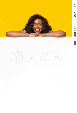 Smiling black woman leaning on white empty board for advertisement Smiling black woman leaning on white empty board for advertisement 70659257