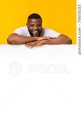 Happy black man leaning on white empty board for advertisement Happy black man leaning on white empty board for advertisement 70659283