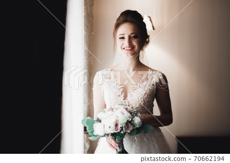 Beautiful bride wearing fashion wedding dress with feathers with luxury delight make-up and hairstyle, studio indoor photo shoot 70662194