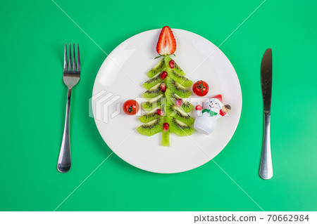 Christmas tree of vegetable and fruit; Kiwi, Strawberry and Pomegranate seed with fork and knife on green background. Merry Xmas and happy New Year party, New You, Healthy food and vegetarian 70662984