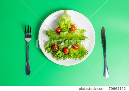 Christmas tree of organic vegetable; frillice iceberg and cherry tomato with fork and knife on green background. Merry Xmas and happy New Year party, New You, Healthy food and vegetarian concept Christmas tree of organic vegetable; frillice iceberg and cherry tomato with fork and knife on green background. Merry Xmas and happy New Year party, New You, Healthy food and vegetarian concept 70663132