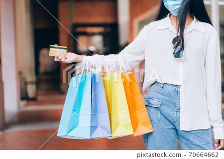Portrait of Asian girl excited beautiful girl wearing protective mask happy smiling with holding credit card and shopping bags enjoying in shopping relaxed expression, lifestyle concept Portrait of Asian girl excited beautiful girl wearing protective mask happy smiling with holding credit card and shopping bags enjoying in shopping relaxed expression, lifestyle concept 70664662
