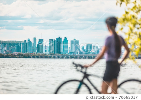 Montreal biking woman cyclist with bike looking at skyline view of condo towers and buildings downtown against Mount Royal landscape. Summer outdoor cycling sport active lifestyle 70665017