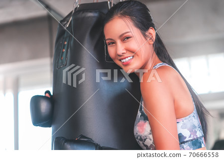 Asian woman is hugging boxing bag with smile while training in fitness gym for happy healthy lifestyle concept. 70666558