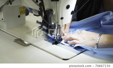 Sewing on machine, close up of hands and blue cloth 70667150