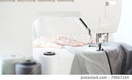 Sewing grey cloth on a white sewing machine, female hands 70667284