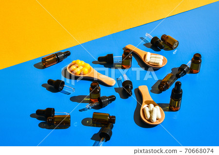 Pills on wooden spoon and dropper pipette on blue and yellow background. Hard light and shadows. Modern isometric creative minimalism concept. Vitamins and prebiotics, probiotics. Dose Pills on wooden spoon and dropper pipette on blue and yellow background. Hard light and shadows. Modern isometric creative minimalism concept. Vitamins and prebiotics, probiotics. Dose 70668074