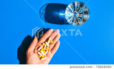 A pile of multi-colored pills in a female hand. A woman holds pills in her hand. The concept of medicine, illness, health. Glass of water. Creative concept. A pile of multi-colored pills in a female hand. A woman holds pills in her hand. The concept of medicine, illness, health. Glass of water. Creative concept. 70668099