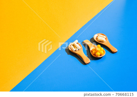 Pills on wooden spoon on blue and yellow background. Hard light and shadows. Modern isometric creative minimalism concept. Vitamins and prebiotics, probiotics. Dose Pills on wooden spoon on blue and yellow background. Hard light and shadows. Modern isometric creative minimalism concept. Vitamins and prebiotics, probiotics. Dose 70668115