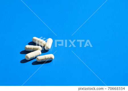 White capsule pills on blue background with hard light and shadows. Copy space for text. Medicine. Healthcare vitamins and prebiotics. White capsule pills on blue background with hard light and shadows. Copy space for text. Medicine. Healthcare vitamins and prebiotics. 70668334