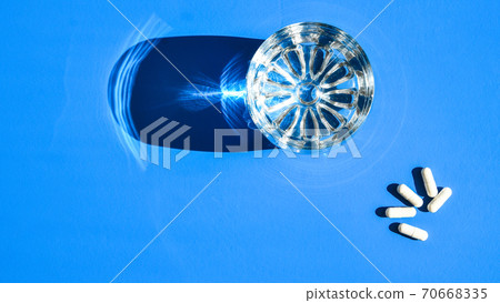 Glass of water and white pills on blue background with hard light and shadows. Creative. White tablets and drink on blue background. Vitamins and prebiotics Glass of water and white pills on blue background with hard light and shadows. Creative. White tablets and drink on blue background. Vitamins and prebiotics 70668335