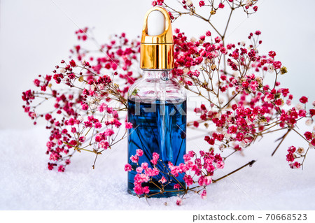 Glass dropper of cosmetic oil and dried flowers and herbs on white background. Natural organic herbal skin care oil, white towel, small pink flowers. 70668523
