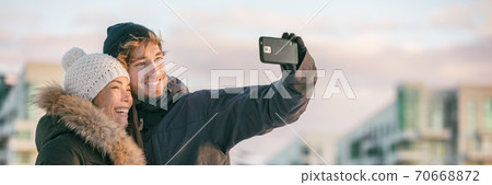 Winter selfie couple tourists on city travel vacation taking photo with mobile phone in street panoramic banner. Happy Asian woman, Caucasian man on holiday Winter selfie couple tourists on city travel vacation taking photo with mobile phone in street panoramic banner. Happy Asian woman, Caucasian man on holiday 70668872