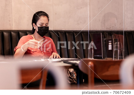 Woman with protective mask in restaurant with menu with partition on table. 70672409