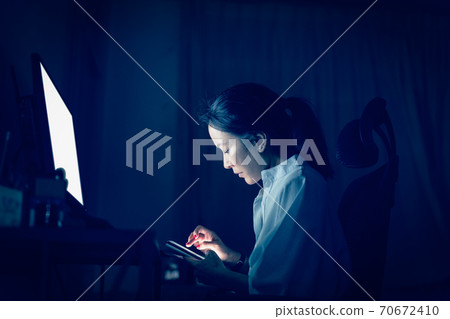 Businesswoman using cell phone while working on the computer late at night. Businesswoman using cell phone while working on the computer late at night. 70672410