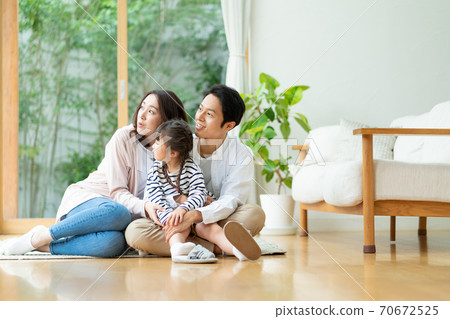 Portrait of a family of three sitting on the floor of the living room and looking into the distance Portrait of a family of three sitting on the floor of the living room and looking into the distance 70672525