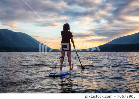 Woman Paddleboarding on Scenic Lake at Sunset 70672903